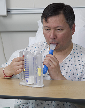 Man in hospital bed using incentive spirometer.